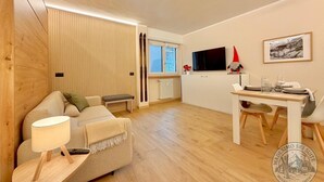 A modern living room with a sofa, a dining table, a TV, and a ski-themed decoration. - "Madesimo Ski Suite": apartment just steps from the slopes! (Madesimo)