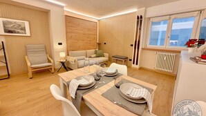 A modern living room with a dining area, a sofa, a chair, a table set for two, and a window with a view. - "Madesimo Ski Suite": apartment just steps from the slopes! (Madesimo)