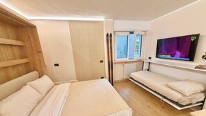 A compact room with a bed, a TV, and a window with curtains. - "Madesimo Ski Suite": apartment just steps from the slopes! (Madesimo)
