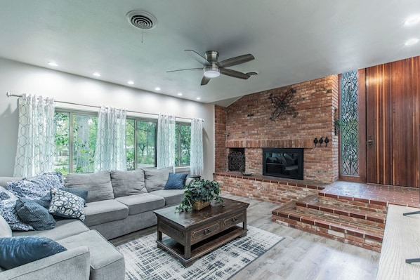 A modern living room with a brick fireplace, a ceiling fan, and a large window with curtains. - Marlandwood a Serene 5-Bed Estate & 3.5 Acres (Temple)