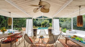 A covered patio with a pool, outdoor furniture, and a view of the surrounding greenery.
