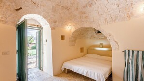Un dormitorio con techo de piedra, una cama con colcha blanca, cabecero de madera y cortina verde.
