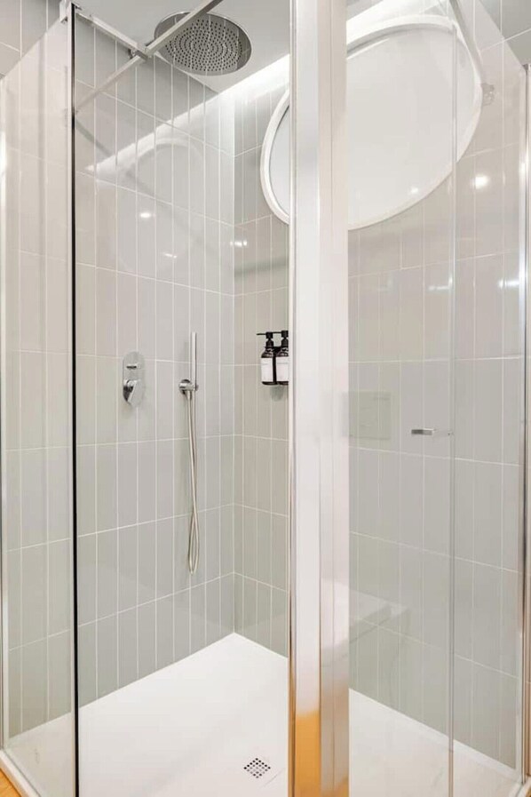 A modern shower enclosure with a glass door, a handheld showerhead, and a wall-mounted faucet.