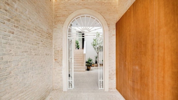 Un couloir aux murs de briques, une porte en bois et une arche blanche menant à un escalier.