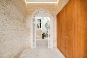 A corridor with brick walls, a wooden door, and a white archway leading to a staircase.