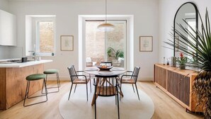 Une cuisine moderne dotée d’un îlot central, d’un coin repas avec une table ronde et d’une grande fenêtre donnant sur un mur de briques.