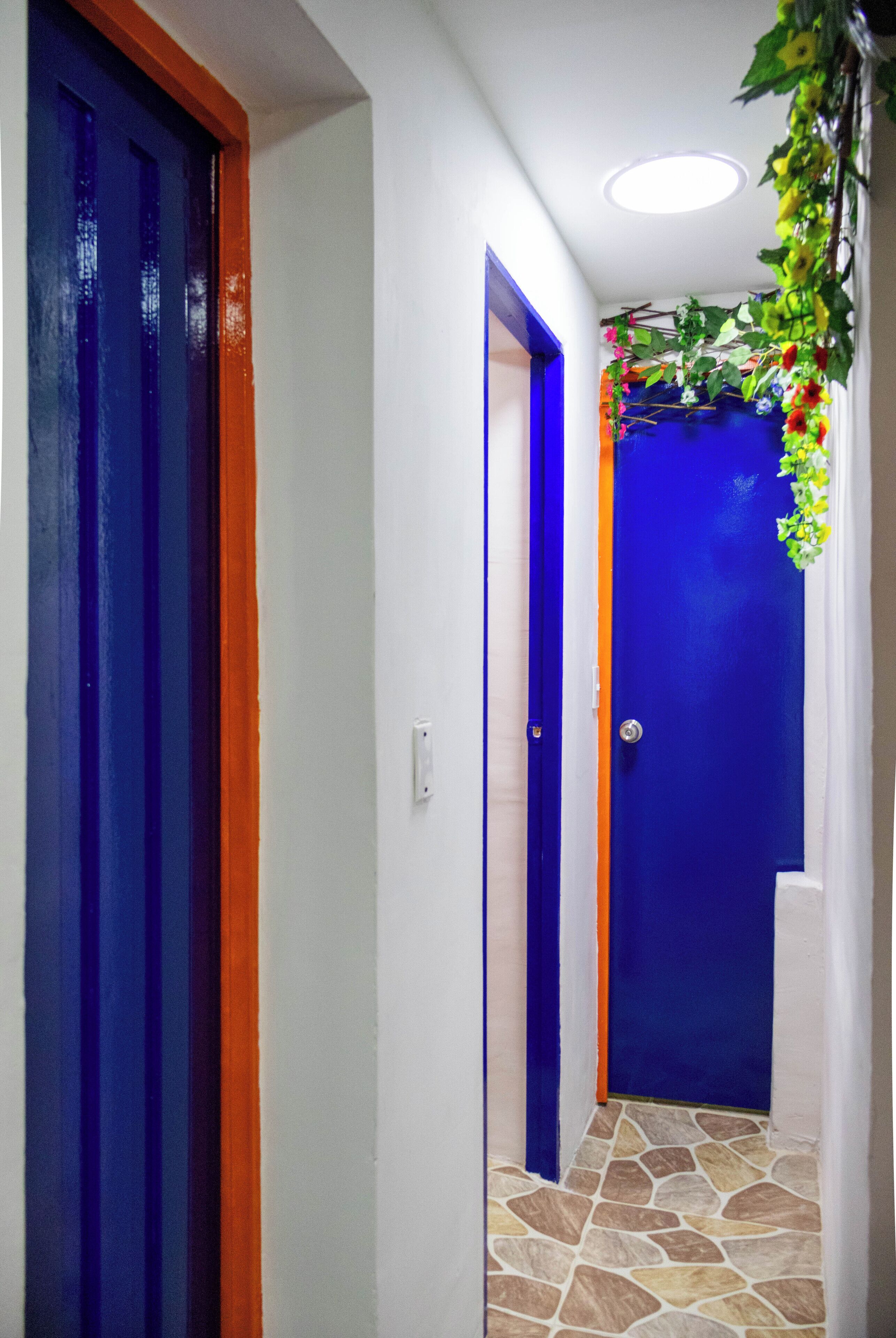 Un couloir avec des portes bleues et oranges, un sol carrelé et un luminaire au plafond.
