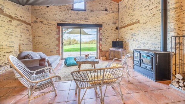 A rustic room with a stone wall, a fireplace, wicker furniture, and a view through a glass door.