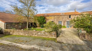 A stone building with a tiled roof, a paved driveway, and a stone wall.