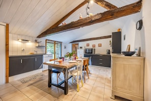 A kitchen with a wooden ceiling, dark cabinets, a dining table with chairs, and a refrigerator.