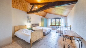 A bedroom with two beds, a wooden ceiling, a balcony with a table, and a view of the outdoors.