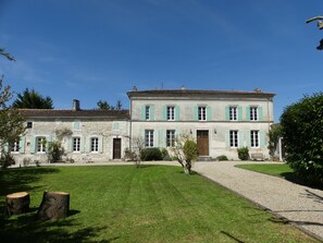 A two-story stone building with a gravel driveway and a well-maintained lawn.