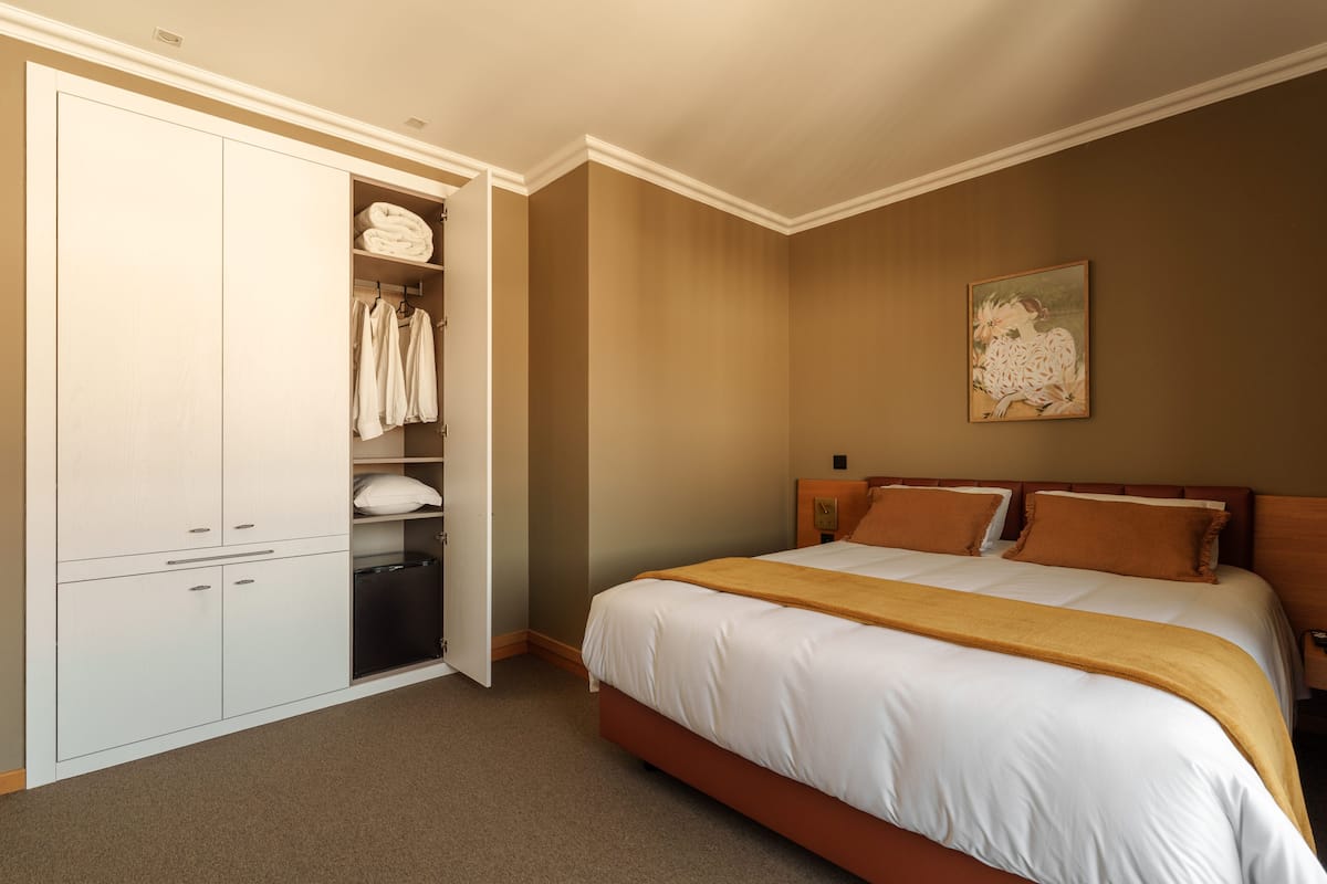 A bedroom with a bed, a wardrobe, and a painting on the wall.