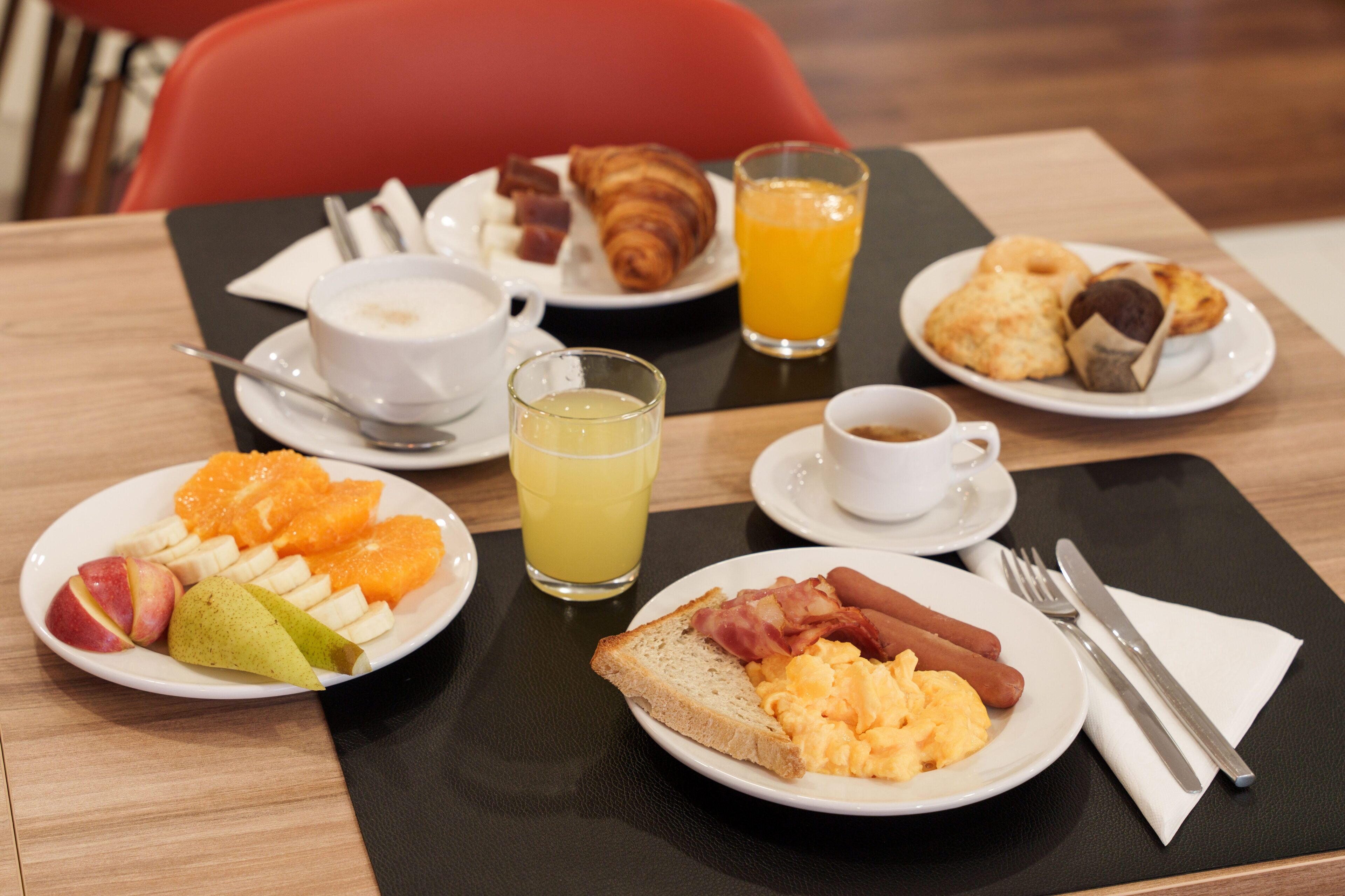 Una mesa de desayuno con platos de comida, un vaso de jugo de naranja y un croissant.