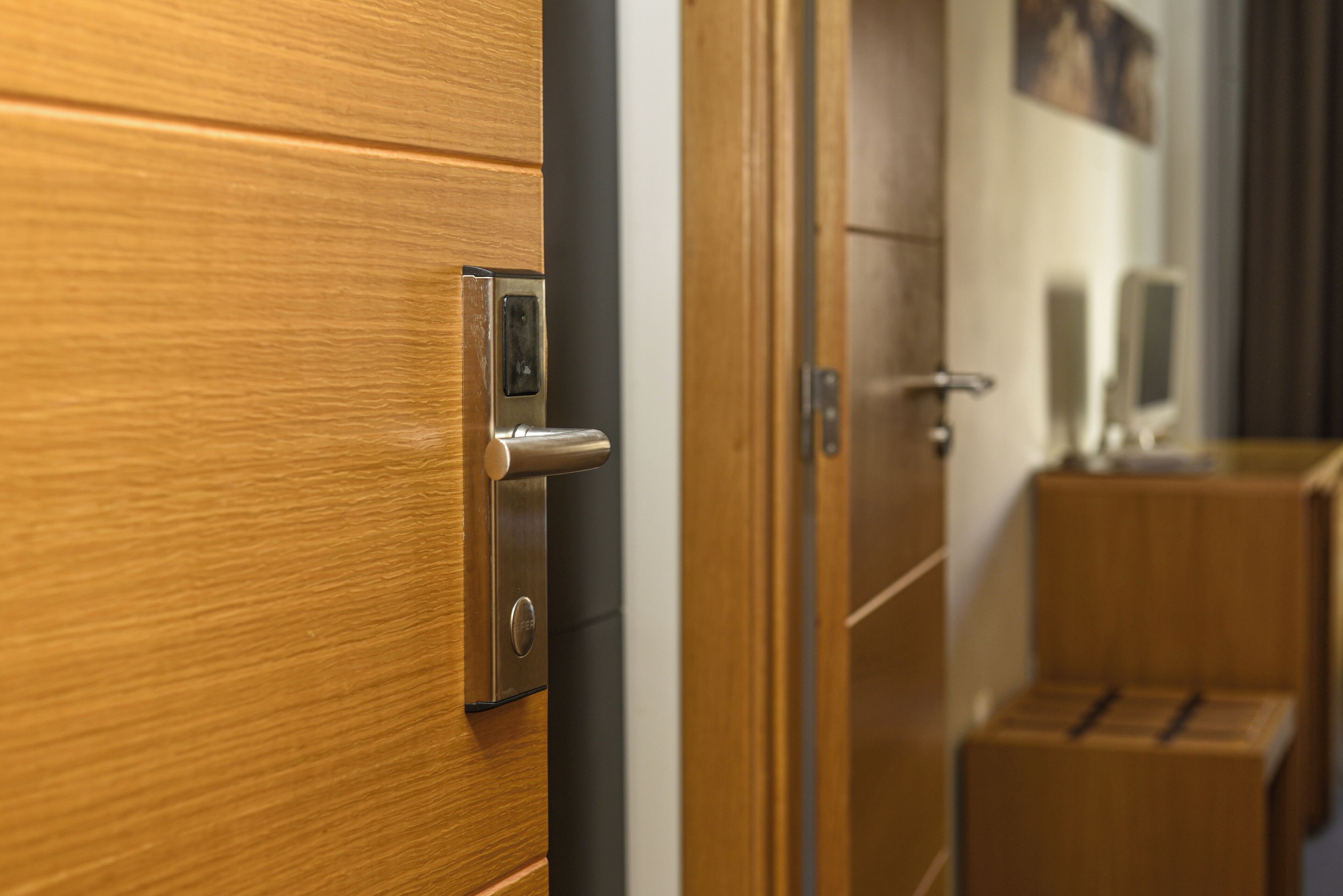 A wooden door with a modern lock and a keyhole, leading to a room with a wooden floor and a small wooden cabinet.