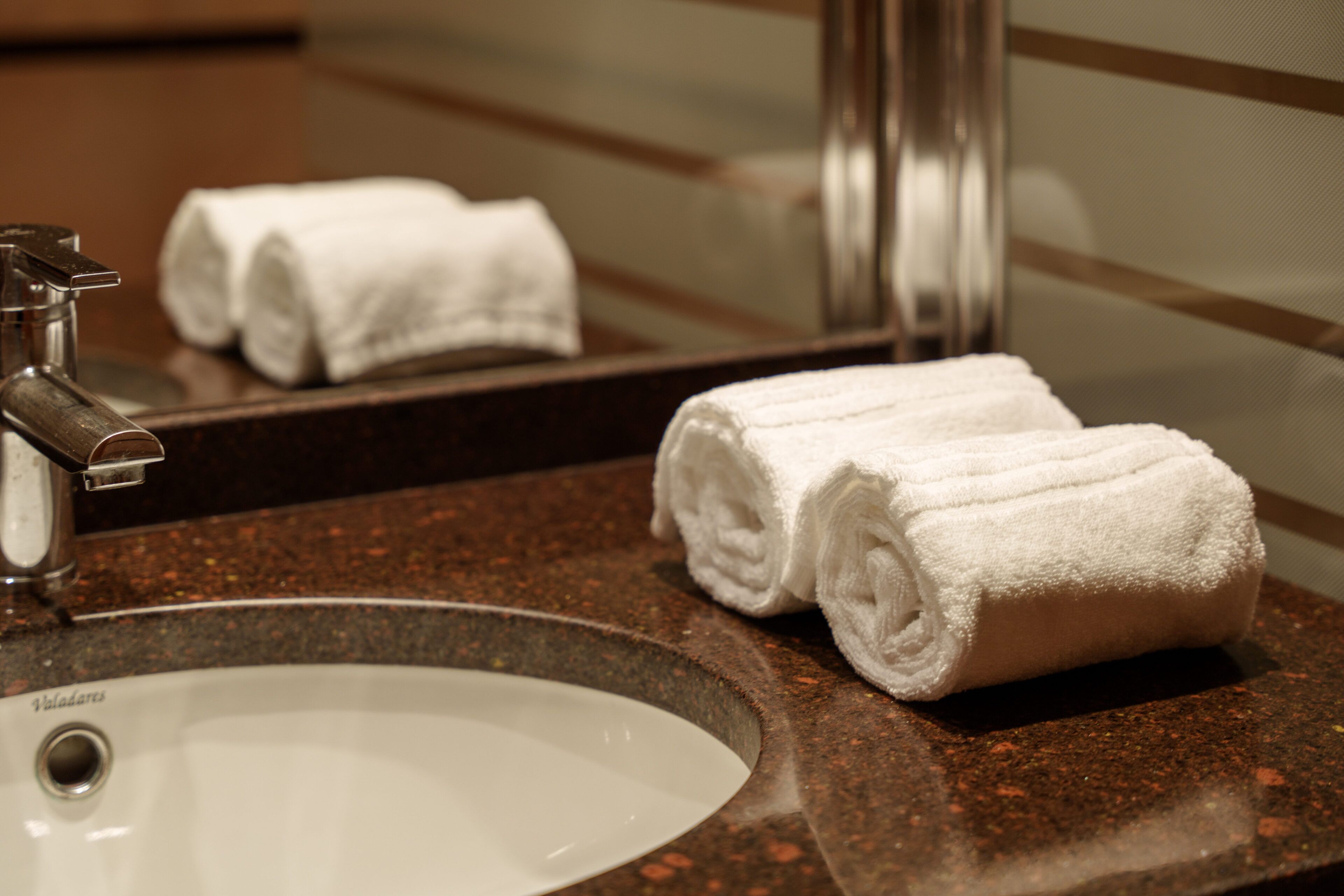 A bathroom with a sink, mirror, and two rolled towels.