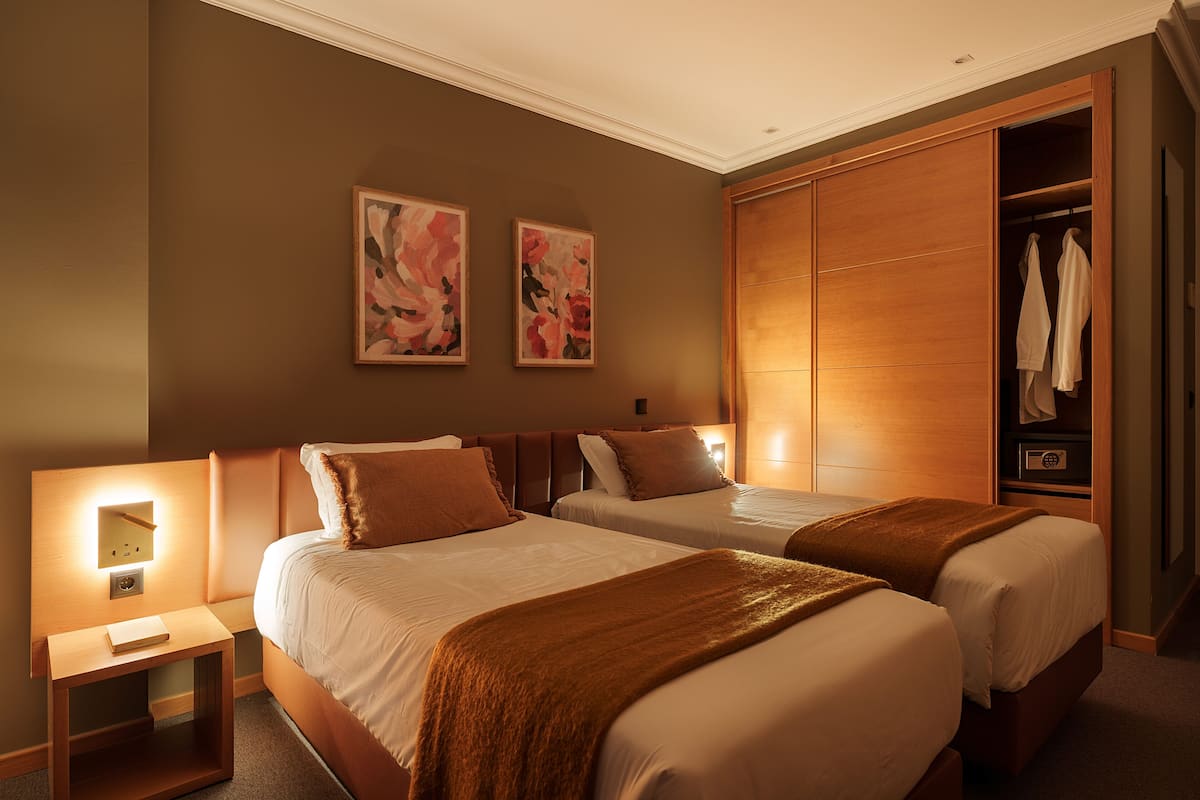 A hotel room with two beds, a wardrobe, and two wall-mounted artworks.