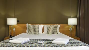 A hotel room with a large bed, two bedside lamps, and a patterned bedspread.