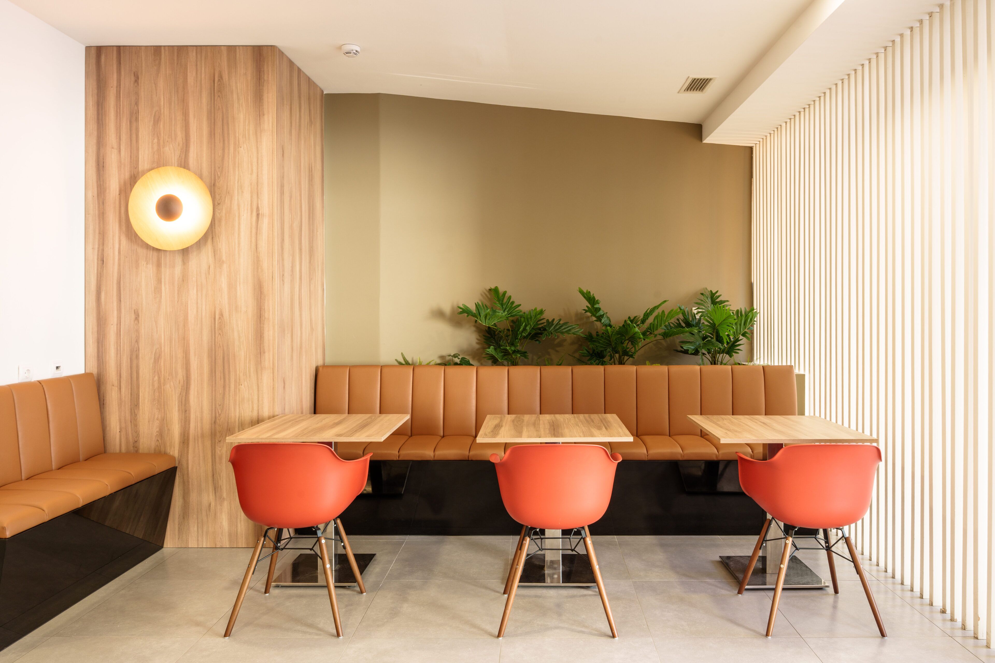 Un interior moderno con un muro decorativo de madera, una zona de estar con un banco y un sofá, y una mesa con sillas.