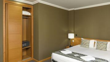 A hotel room with a large bed, a wardrobe with a radio, a bedside table with a lamp, and patterned pillows.