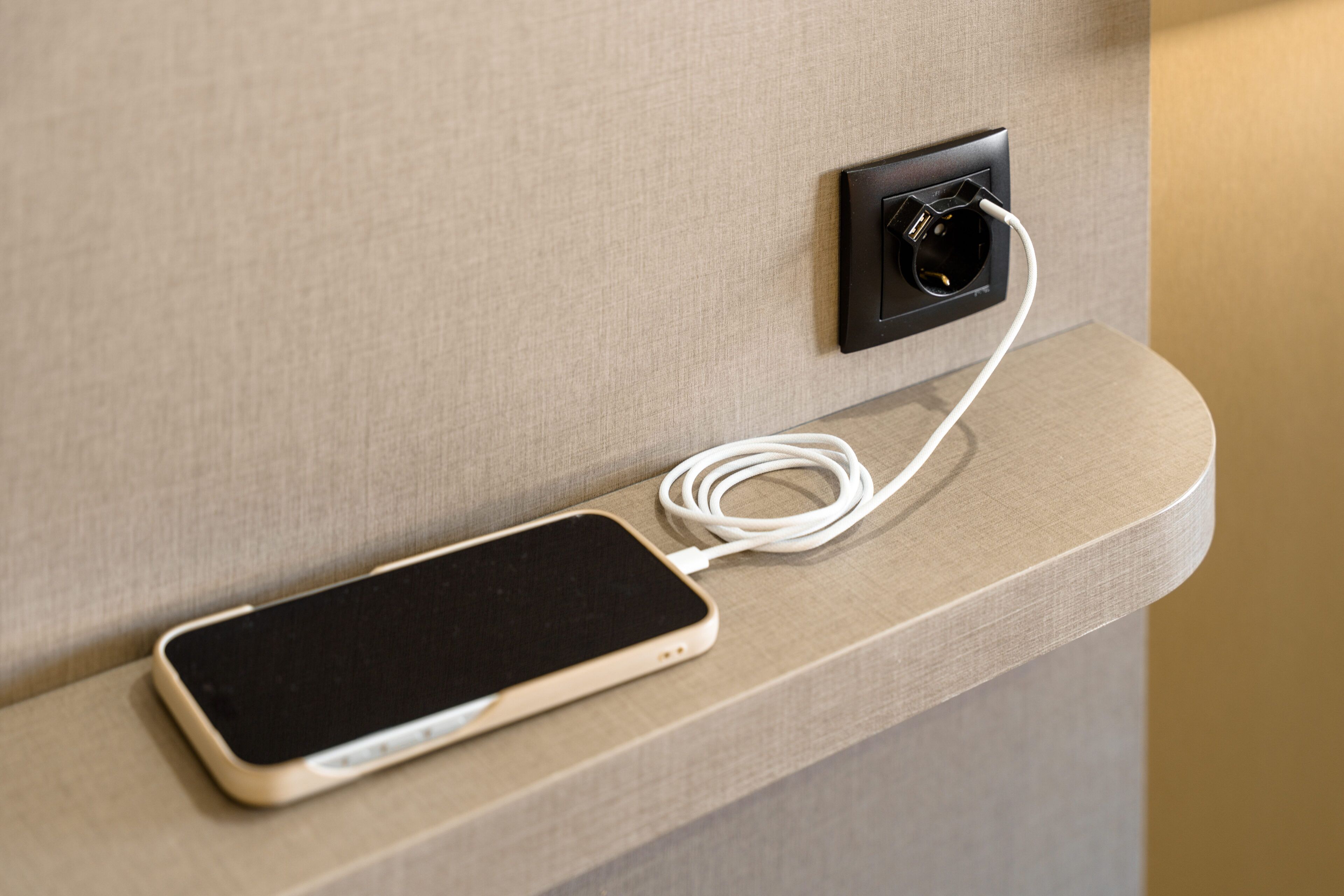 A smartphone connected to a wall socket on a textured wall.