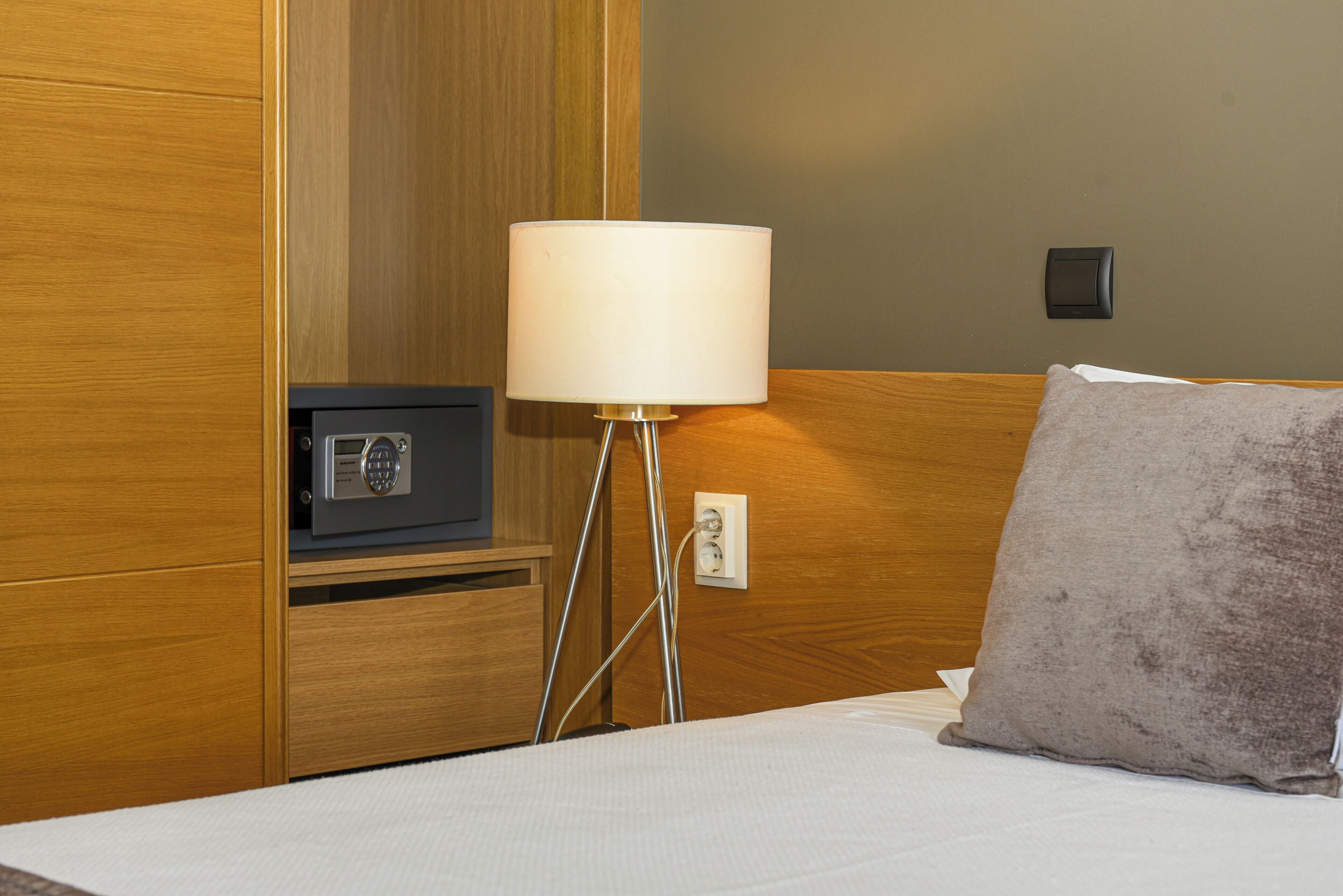 Hotellihuone, jossa on sänky, yöpöytälamppu, radio ja seinäpistorasia.