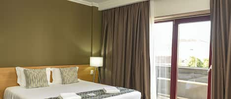 A hotel room with a large bed, a nightstand with a lamp, and a view of the outside through a sliding glass door.
