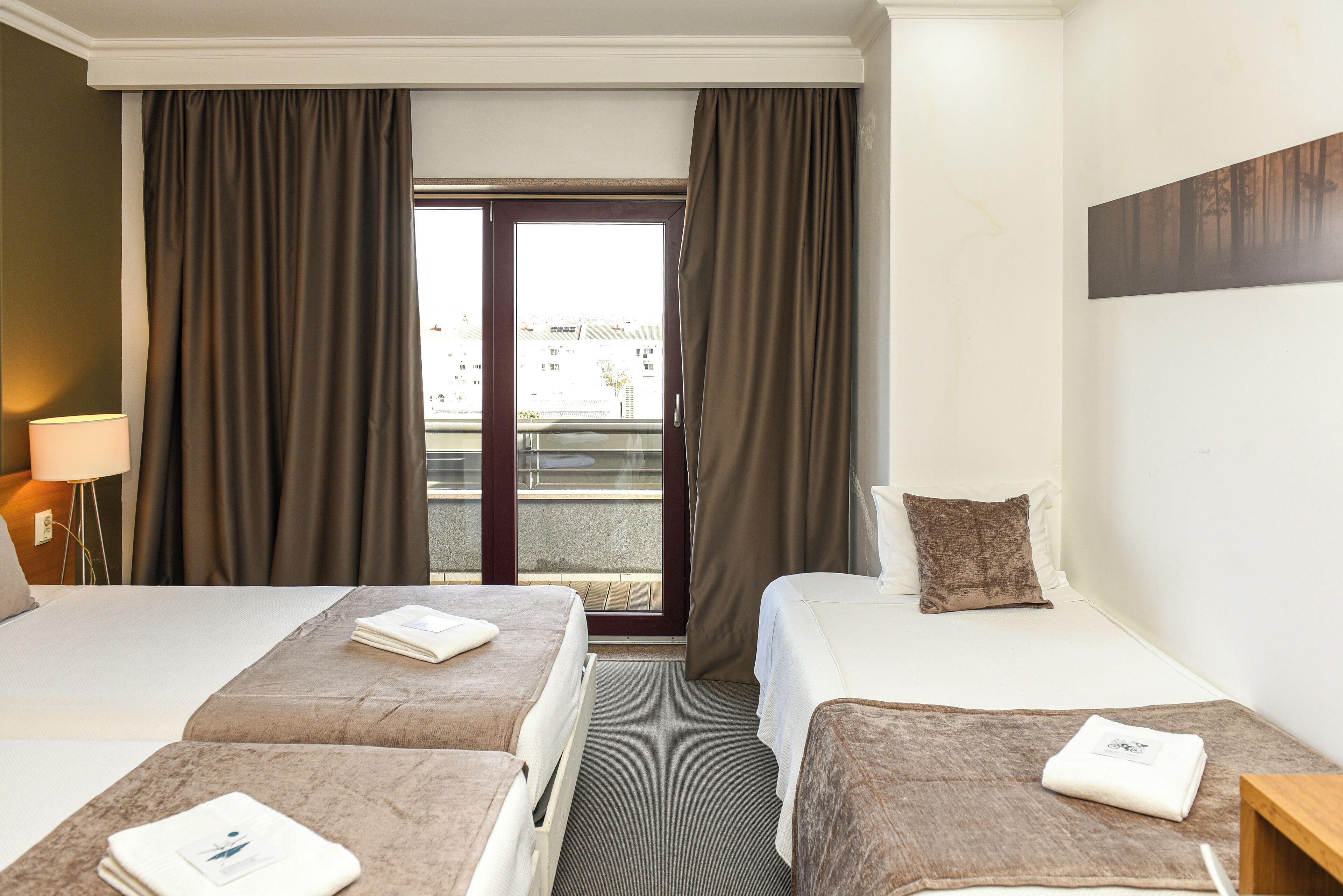 A hotel room with two beds, a balcony, and a view of the city.