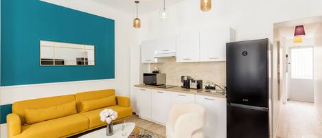 A modern kitchen with white cabinets, a black refrigerator, and a yellow sofa.