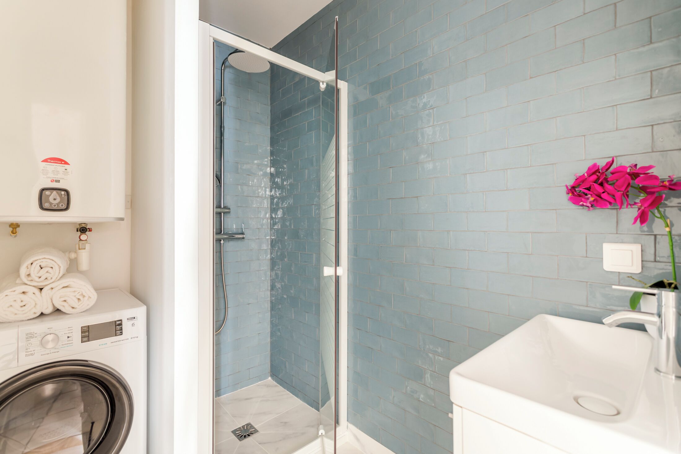 A bathroom with a glass-enclosed shower, a white sink, and a blue-tiled wall.