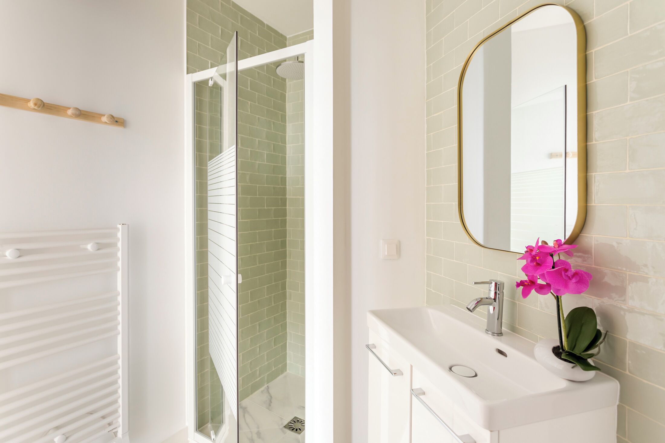 A bathroom with a white sink, a mirror, and a shower area with green tiles.