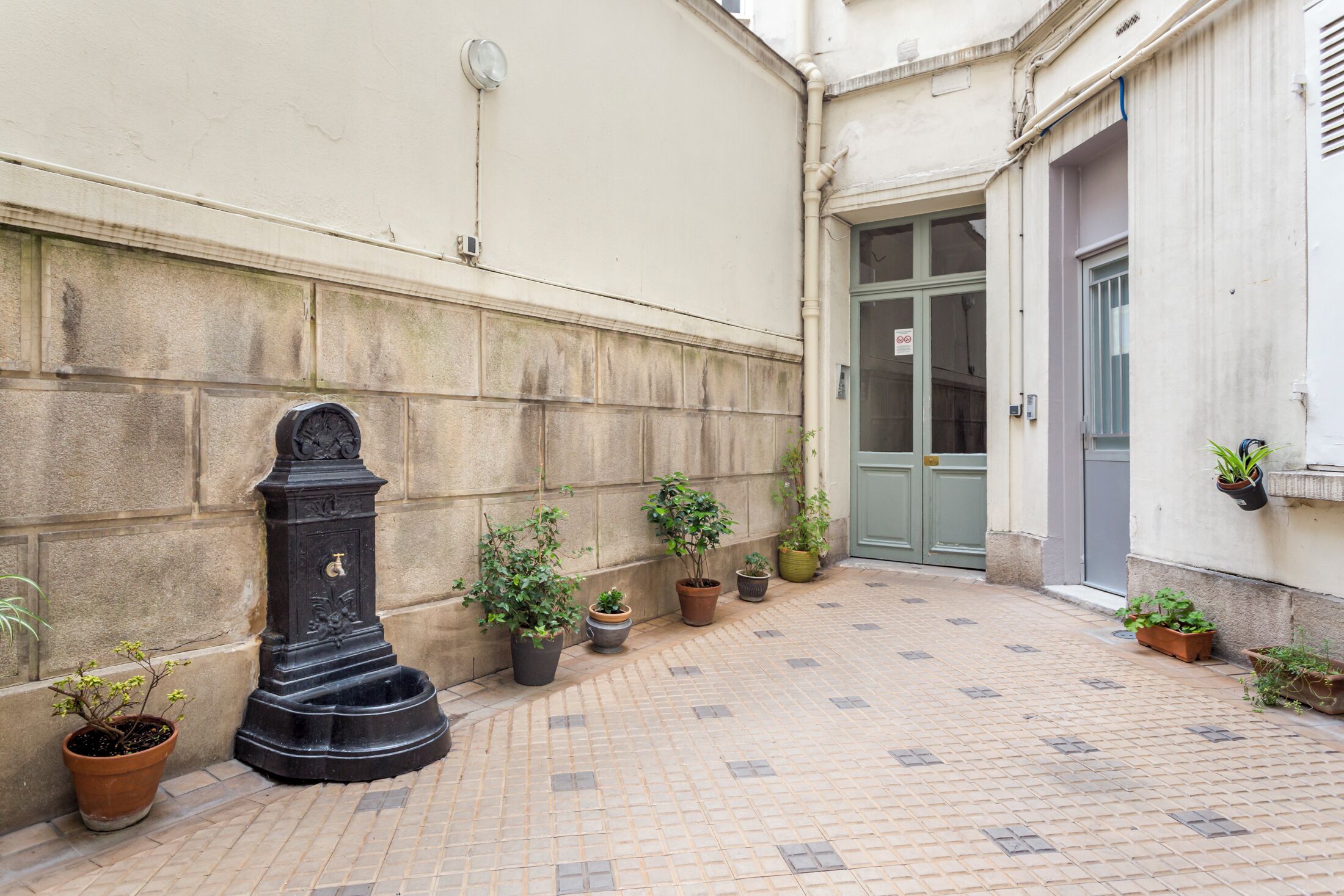 Un cortile con pavimento piastrellato, una colonna nera e piante in vaso.