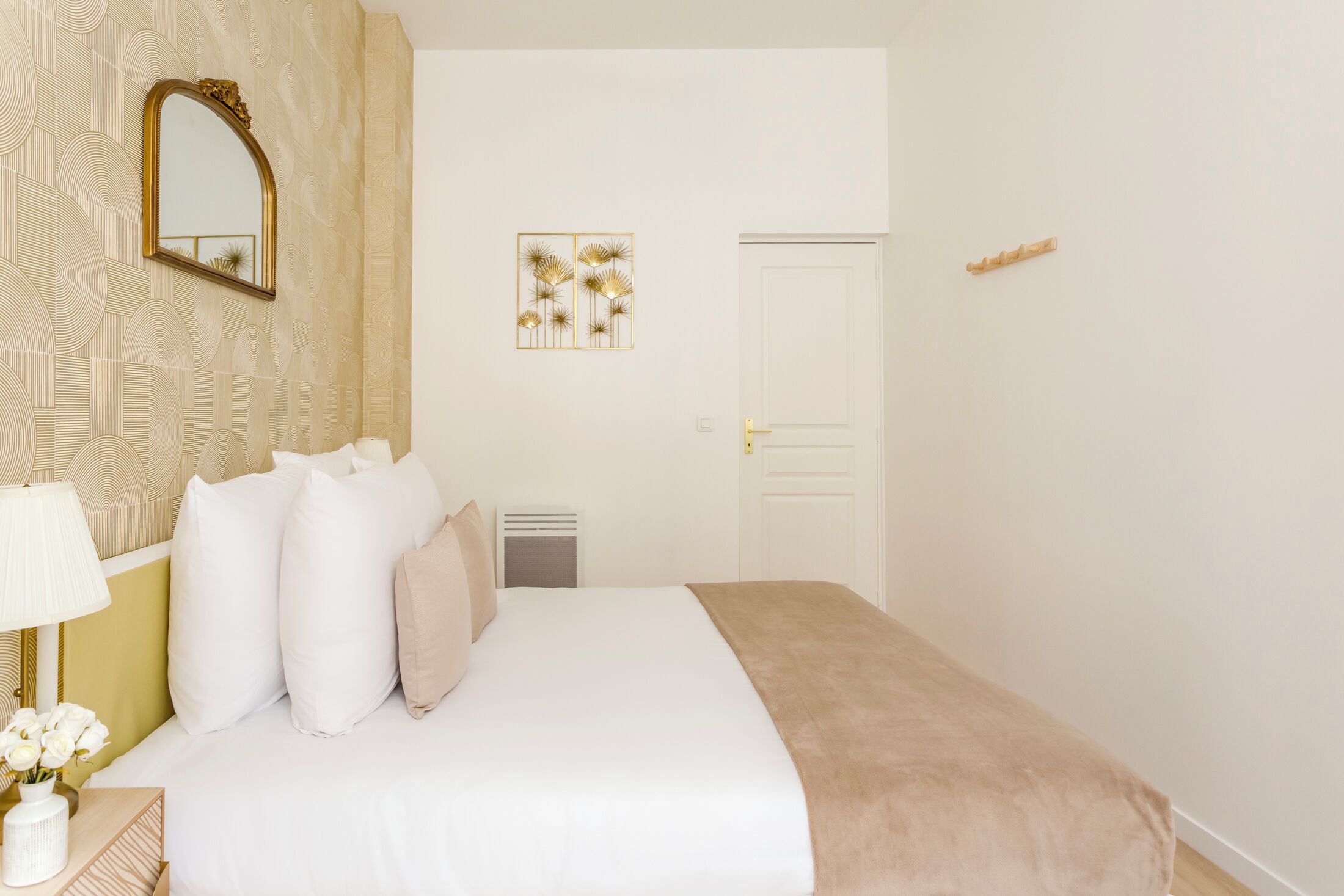 Een keurig opgemaakt slaapkamer met een bed, nachtkastje, lamp en een spiegel.