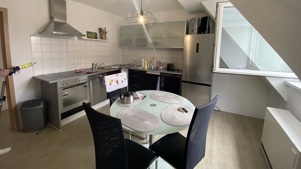 A modern kitchen with a dining area, featuring a round table with placemats, black chairs, and a stainless steel refrigerator.