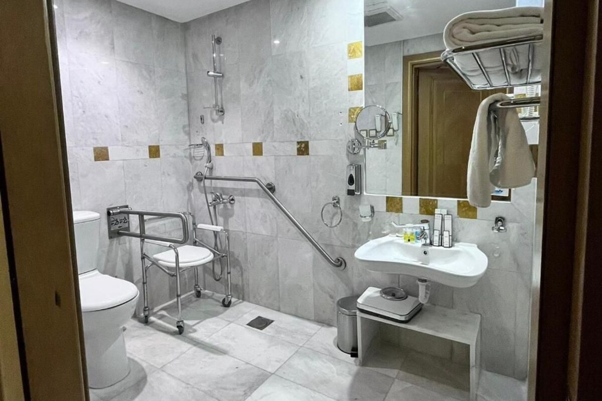 Une salle de bain moderne équipée d’une douche, de toilettes et d’un lavabo, ainsi que d’une barre d’appui et de barres de maintien pour faciliter l’accès aux personnes à mobilité réduite.