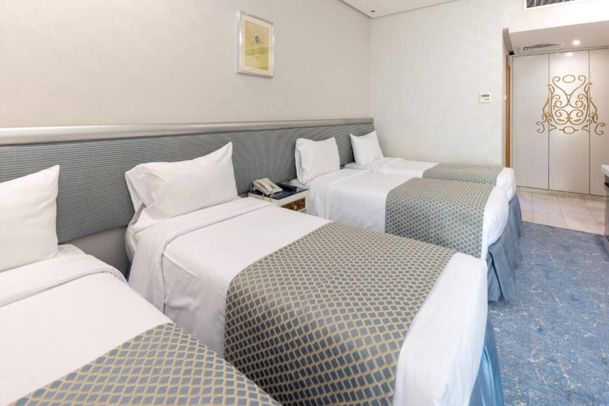 Een hotelkamer met drie bedden, een nachtkastje met telefoon, een lijst met foto aan de muur en een kast met decoratieve handgreep.