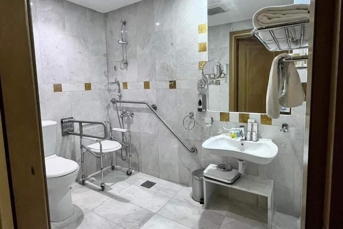 Une salle de bain moderne équipée d’une douche, de toilettes et d’un lavabo, ainsi que d’une barre d’appui et de barres de maintien pour faciliter l’accès aux personnes à mobilité réduite.