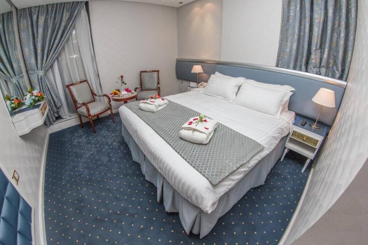 Een hotelkamer met een groot bed, twee nachtkastjes, een stoel en een bijzettafeltje met bloemen.