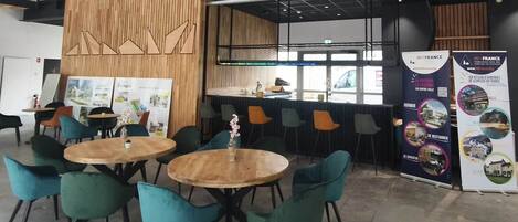 A modern interior with round tables and teal chairs, wooden accents, and a high ceiling.