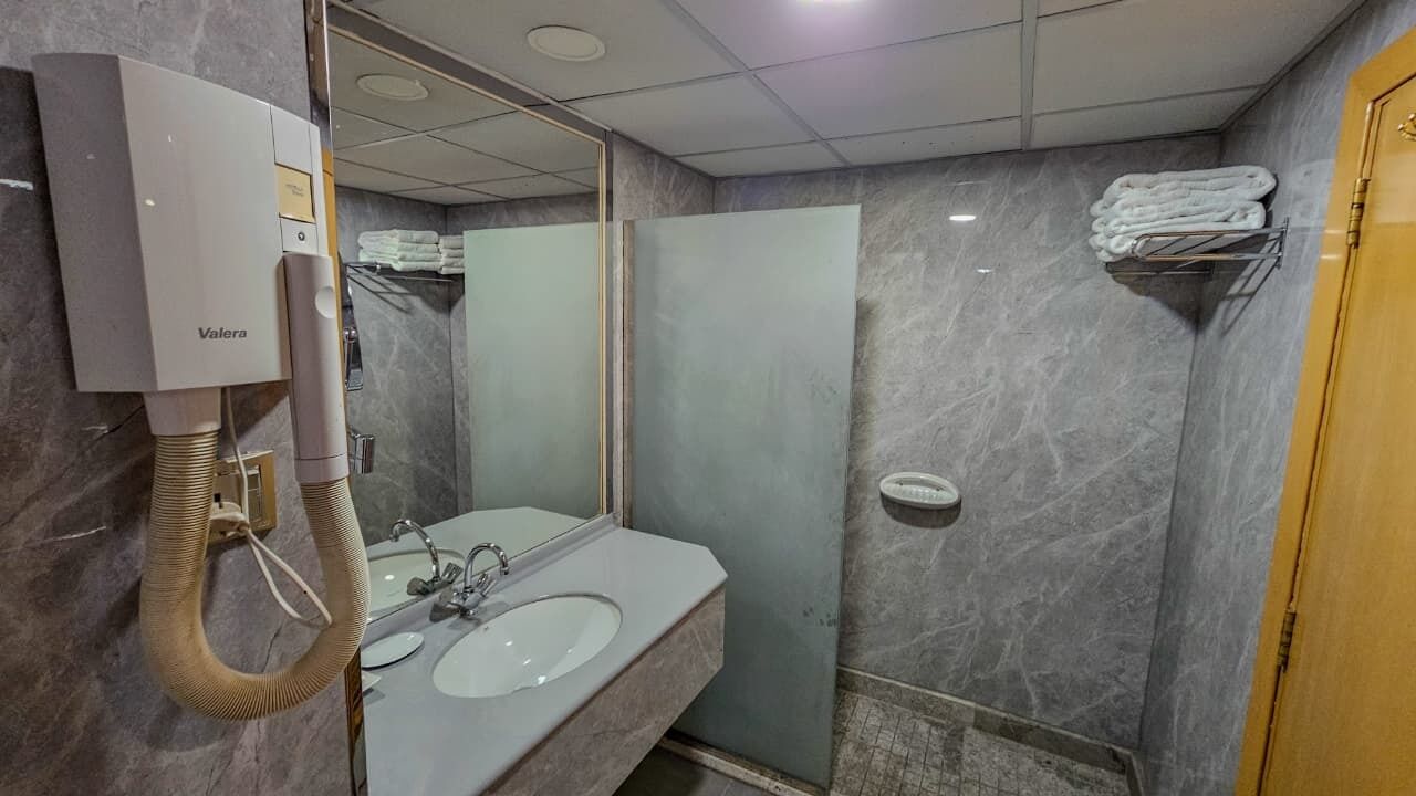 Un baño con calentador de agua Valera, un lavamanos, un espejo y un perchero para toallas.