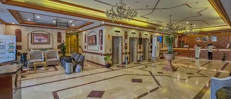 A spacious lobby with a marble floor, a reception desk, a chandelier, and a seating area.