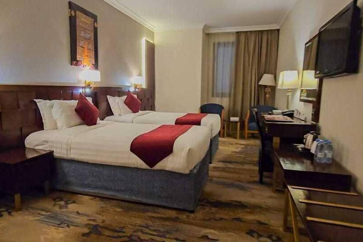 Une chambre d’hôtel avec un grand lit, un bureau, une chaise, une télévision et une fenêtre avec des rideaux.