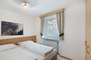 A hotel room with two beds, a painting on the wall, a window with curtains, and a radiator.