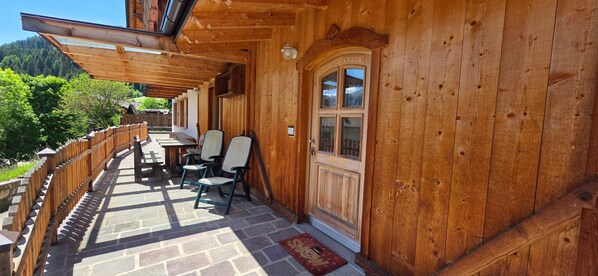 A wooden building with a covered patio, stone flooring, and a door with glass panels.