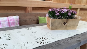 A wooden bench with a floral-patterned tablecloth, a wooden box with a heart-shaped cutout, and a green cushion.