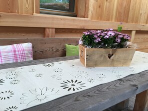 A wooden bench with a floral-patterned tablecloth, a wooden box with a heart-shaped cutout, and a green cushion.