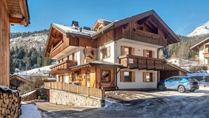 A multi-story wooden building with balconies, a stone wall, and a snow-covered ground.