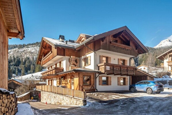 Un bâtiment en bois à plusieurs étages, doté de balcons, d’un mur en pierre et d’un sol recouvert de neige.