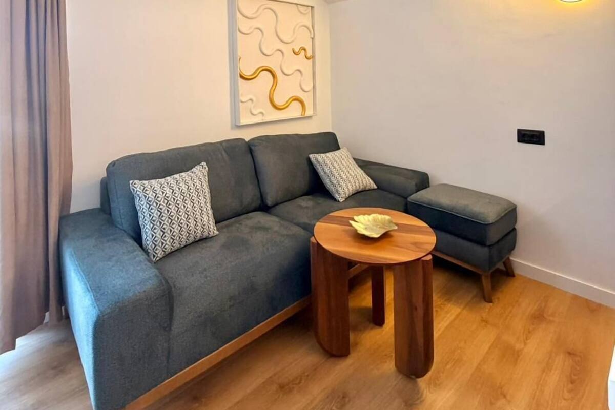 A modern living room with a grey sectional sofa, a small wooden coffee table, and a wall-mounted air conditioning unit.