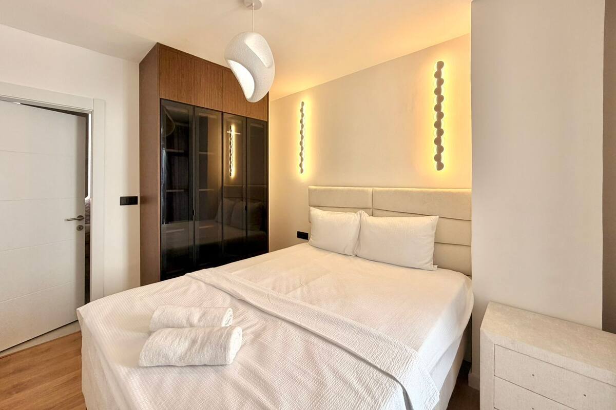 A modern bedroom with a large bed, a wardrobe, and a bedside table.